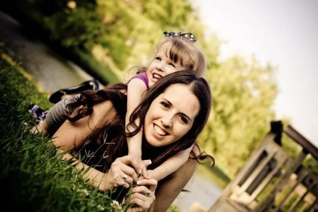 mom laying in the grass with daughter on her back