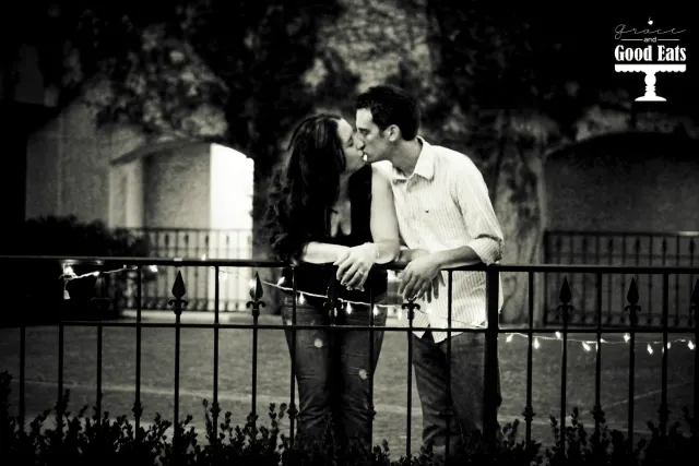 couple kissing against rail with lights strung on it