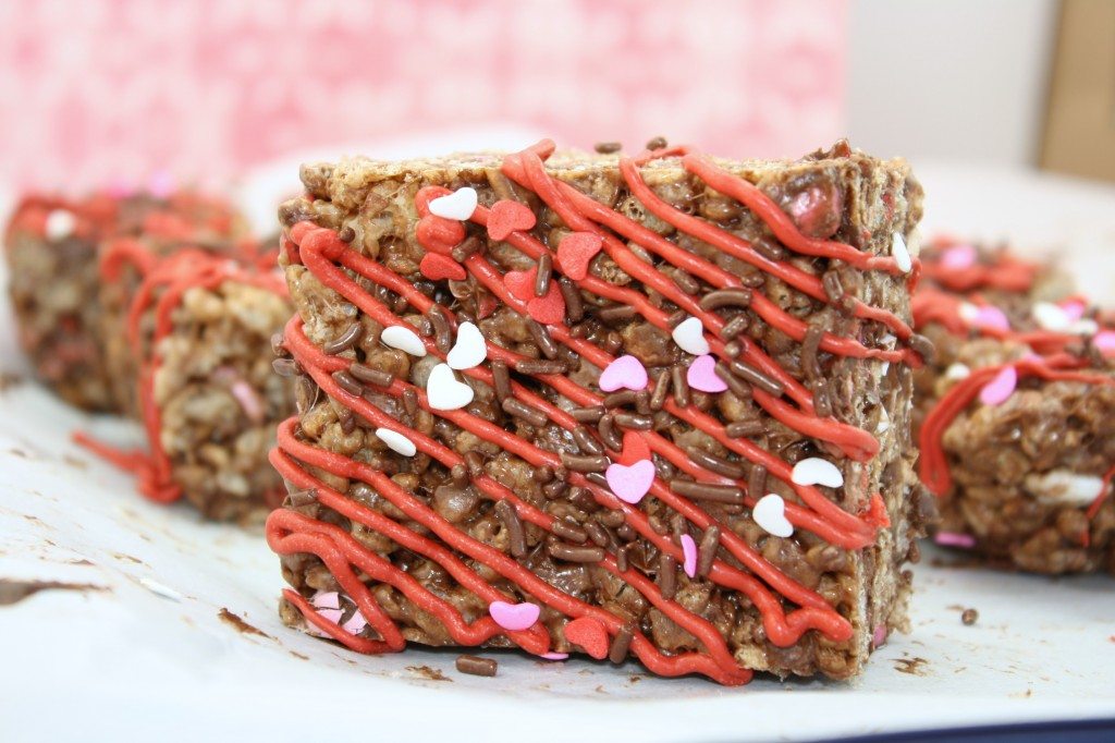 A cocoa krispies treat drizzled with red melting candy and topped with sprinkles. 