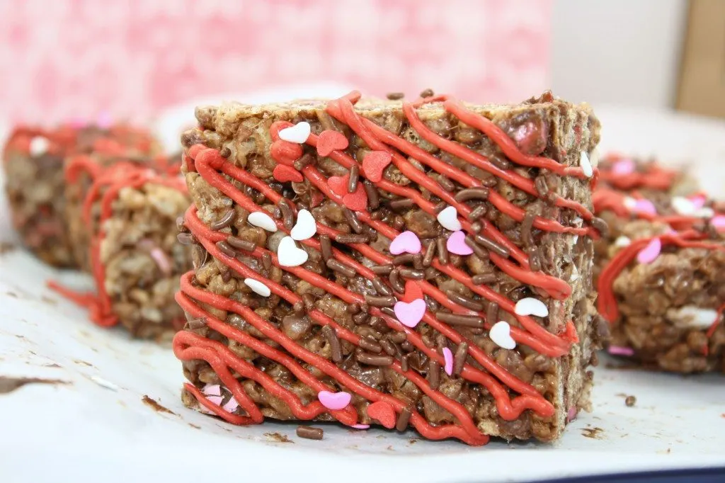A cocoa krispies treat drizzled with red melting candy and topped with sprinkles. 