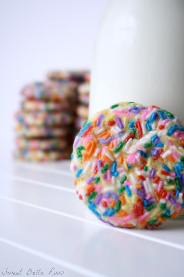 A confetti cookie next to a pitcher of milk. 