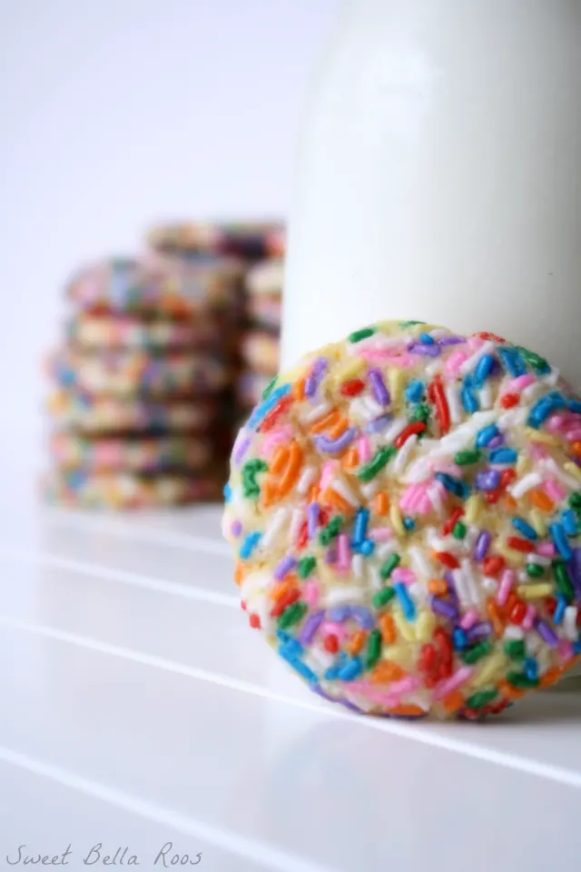 A confetti cookie next to a pitcher of milk. 