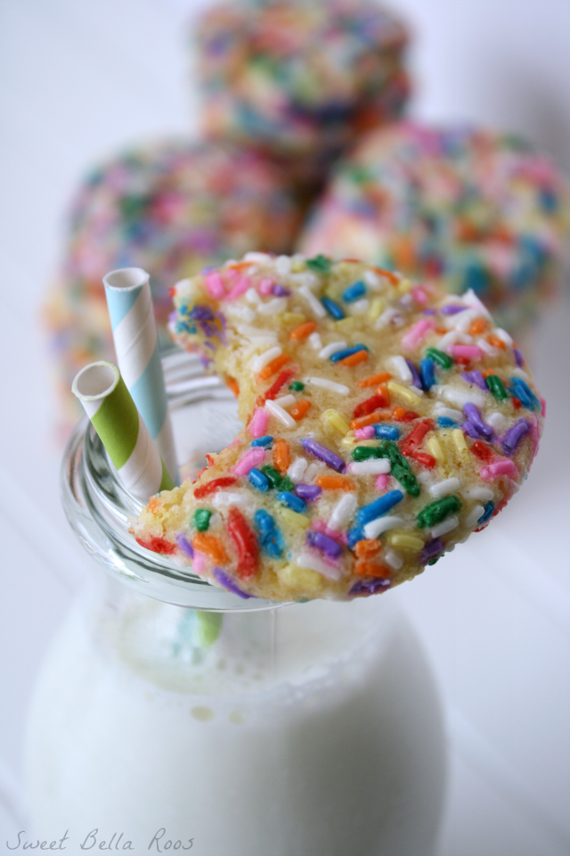 A sprinkle cookie with a bite missing resting on top of a pitcher of milk. 