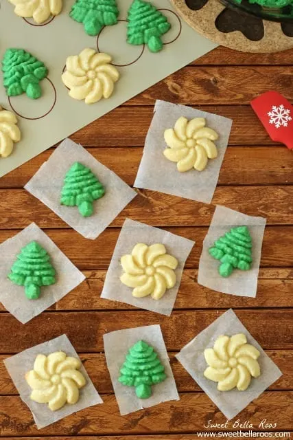Create a new holiday tradition with this classic Spritz Cookies Recipe. Sharing my favorite cookie press as well as instructions for how to make Spritz Cookies without a press. The buttery cookies can be dressed up with sprinkles or different colors of dough. butter spritz cookies shaped as white flowers and green trees