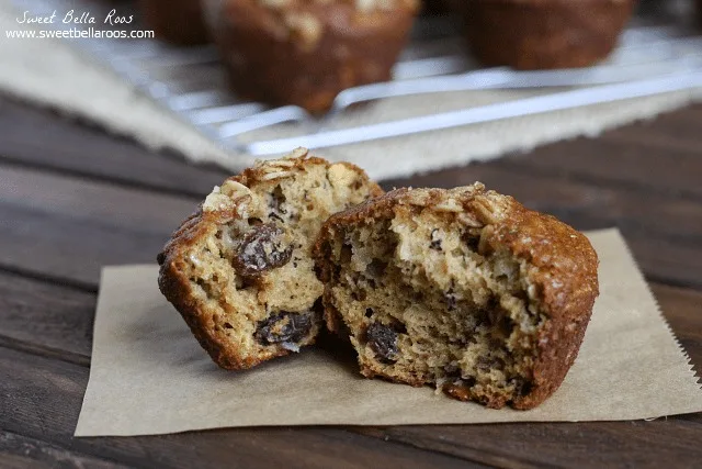 An oatmeal raisin muffin cut in half resting on a square of parchment paper. 