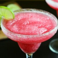 bright red cranberry margarita in a clear glass with salt and lime on the rim