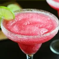 bright red cranberry margarita in a clear glass with salt and lime on the rim