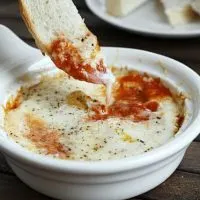 a thin slice of bread being dipped into a dish of Italian Baked Eggs