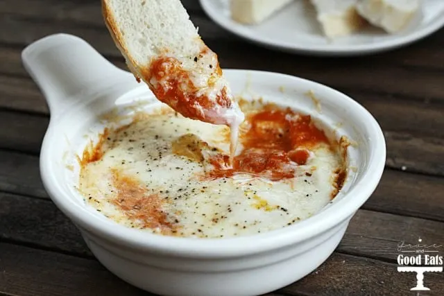 a thin slice of bread being dipped into a dish of Italian Baked Eggs