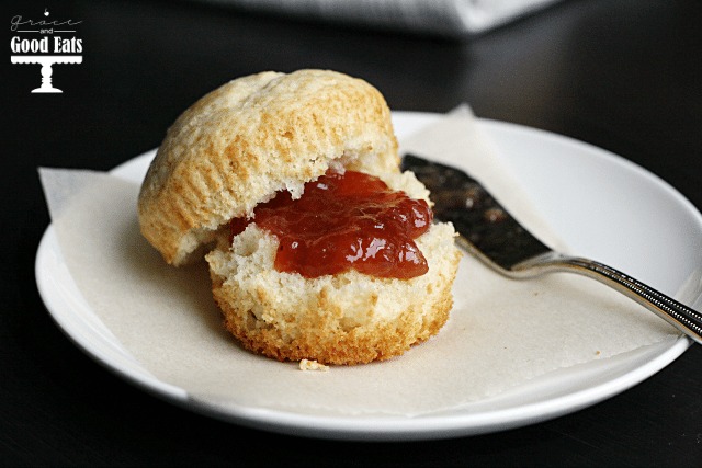 A plain muffin slathered with jam on a white plate. 