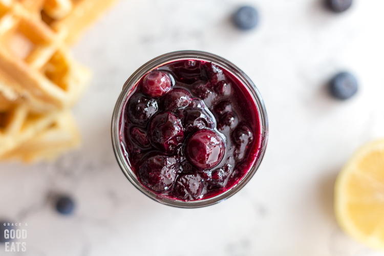 blueberry syrup in a glass jar next to a stack of waffles