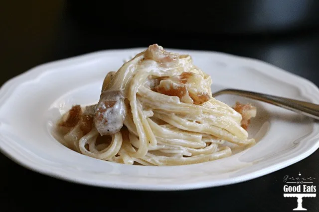 Parmesan prosciutto pasta on a white plate with a fork. 