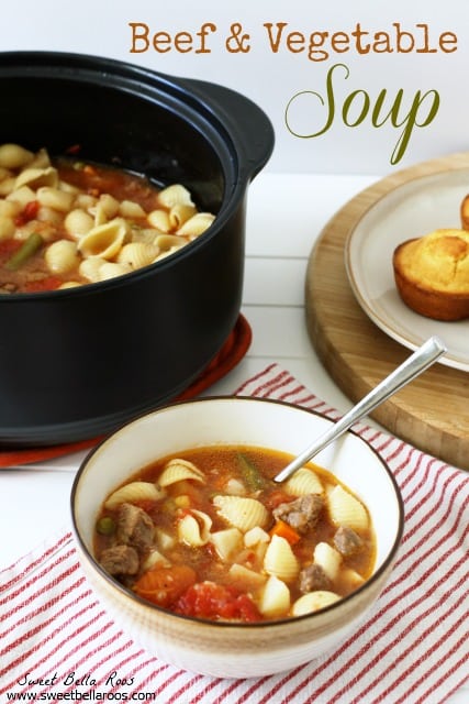 A bowl of beef and vegetable soup. A pot of soup and a plate of cornbread rests in the background. 