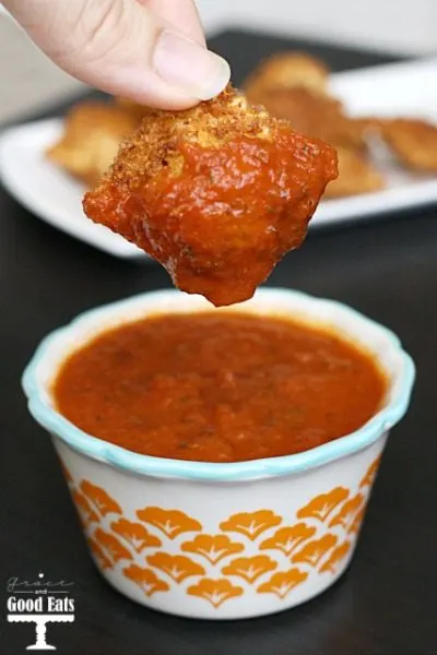 a pan fried ravioli being dunked into marinara sauce