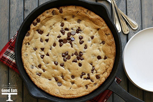 baked cast iron chocolate chip cookie on top of red checked tea towel next to stack of plates