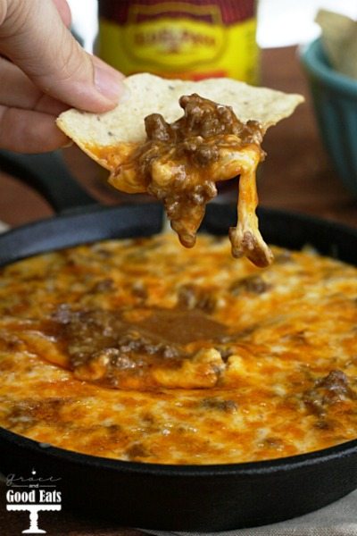 Beef enchilada dip being scooped out of a cast iron skillet with a tortilla chip. 