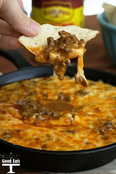 Beef enchilada dip being scooped out of a cast iron skillet with a tortilla chip. 