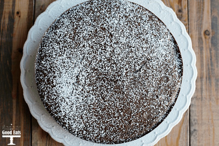 a simple moist chocolate cake dusted with powdered sugar on a white plate 