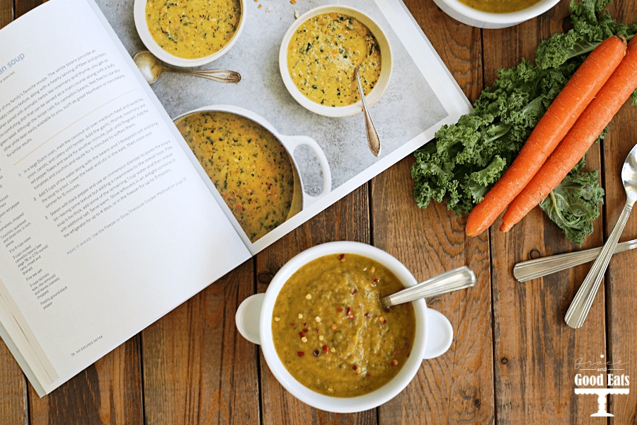 Overhead view of open cookbook, veggies, and a bowl of tuscan white bean kale soup. 