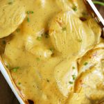 baking dish of scalloped potatoes covered in cheese and topped with green onions