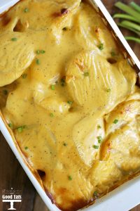 baking dish of scalloped potatoes covered in cheese and topped with green onions