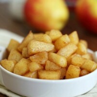sautéed cinnamon apples in a small white dish with apples and cinnamon in the background
