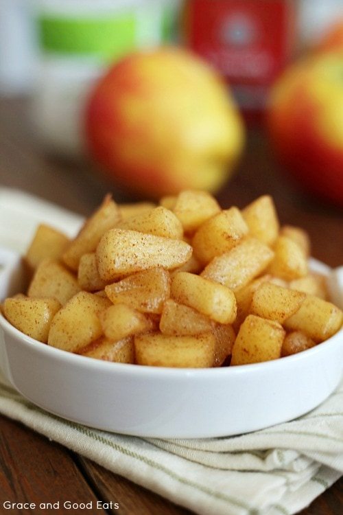 sautéed cinnamon apples in a small white dish with apples and cinnamon in the background 