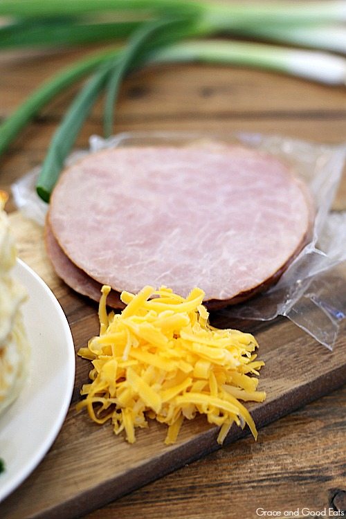 sliced ham and shredded cheese on a wood cutting board