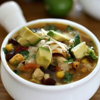 instant pot chicken tortilla soup with beans, corn, chicken, and tomatoes topped with cheese, corn chips, and avocados