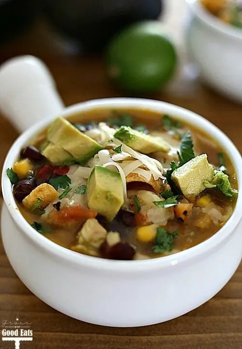 instant pot chicken tortilla soup with beans, corn, chicken, and tomatoes topped with cheese, corn chips, and avocados