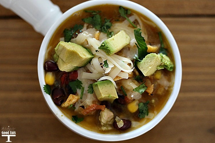 white bowl of Chicken Tortilla Soup topped with cheese and avocados