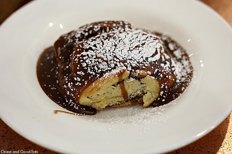 cinnamon roll covered in caramel sauce and powdered sugar on a large white plate