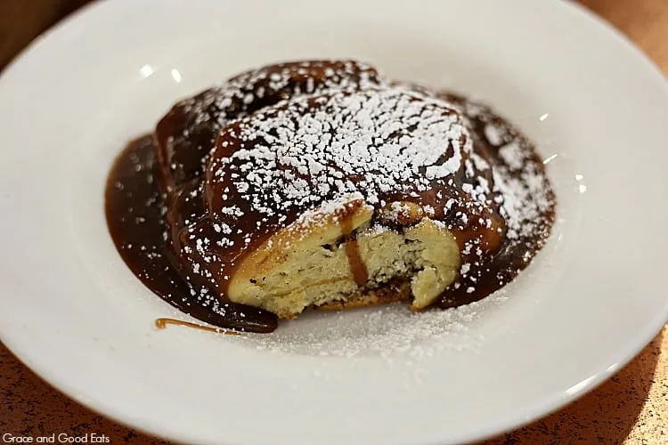 cinnamon roll covered in caramel sauce and powdered sugar on a large white plate