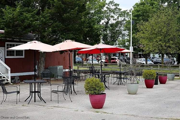 outdoor patio tables with red umbrellas surrounded by trees and potted plants