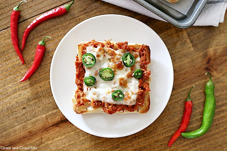 white plate with tuna melt surrounded by red and green peppers on a brown table