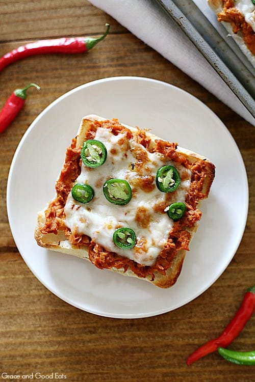 overhead view of a square ciabatta roll topped with tuna, cheese, and green jalapenos on a round, white plate