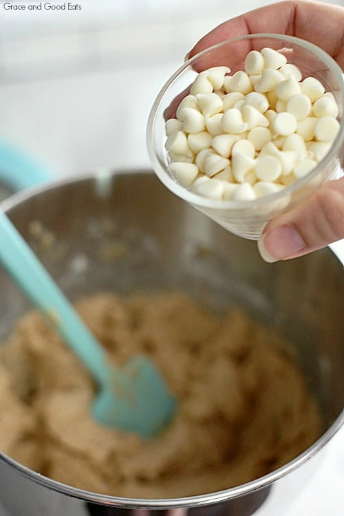 pouring white chocolate chips into cookie batter