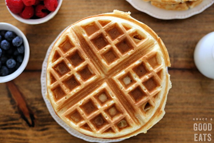 fluffy waffle on plate next to bowls of berries