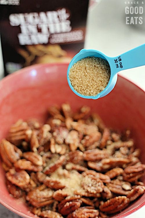 adding turbinado sugar to a bowl of pecans