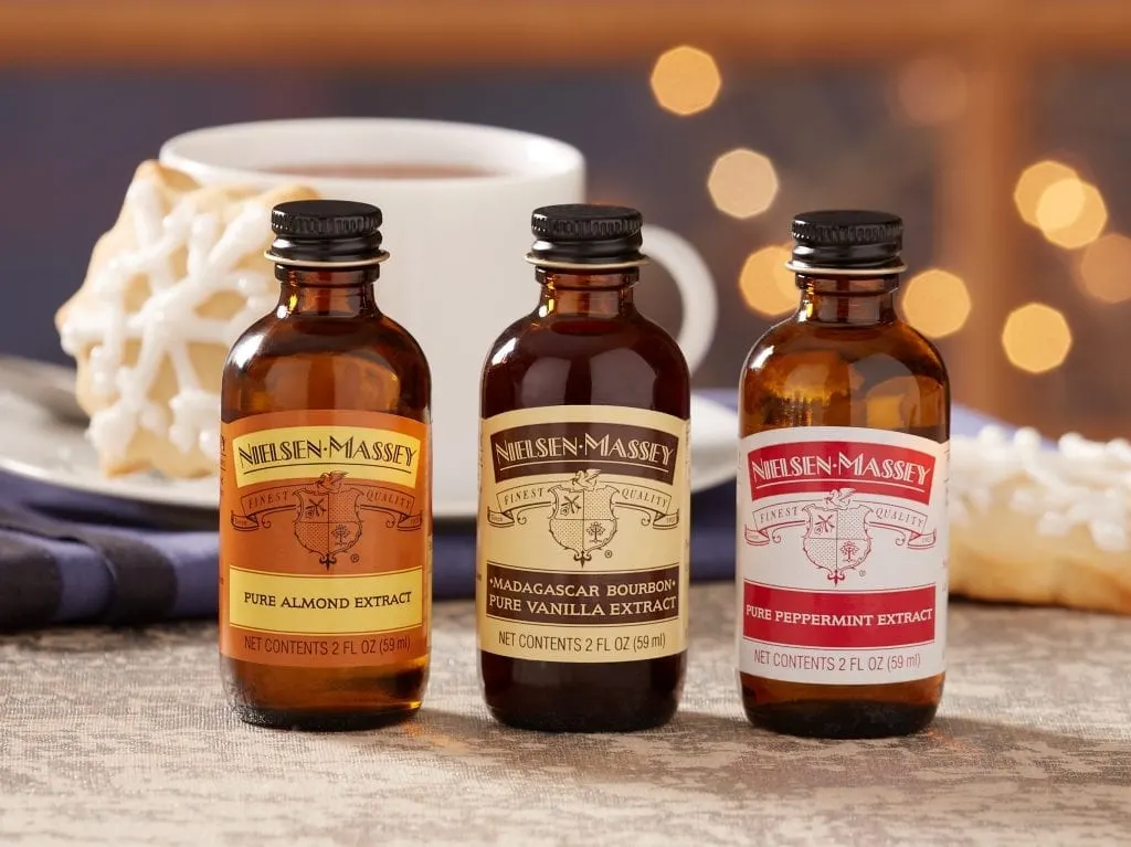 three bottle of Nielsen-Massey extracts in front of a cup of coffee and sugar cookie