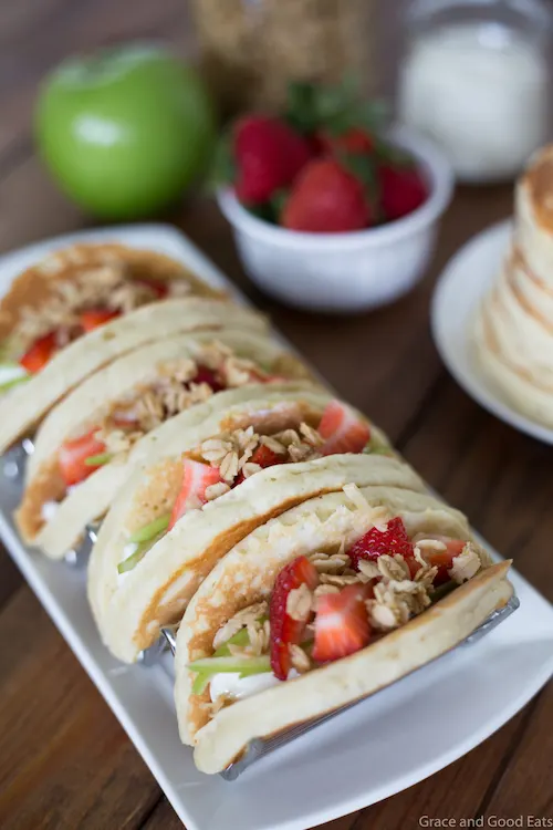 Pancake Parfait Tacos filled with yogurt, granola, apples, and strawberries and topped with a drizzle of honey.  Serve with breakfast potatoes or scrambled eggs for an easy, kid-friendly breakfast!