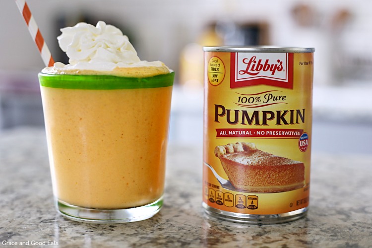a glass of pumpkin smoothie with whipped cream next to a can of pumpkin puree