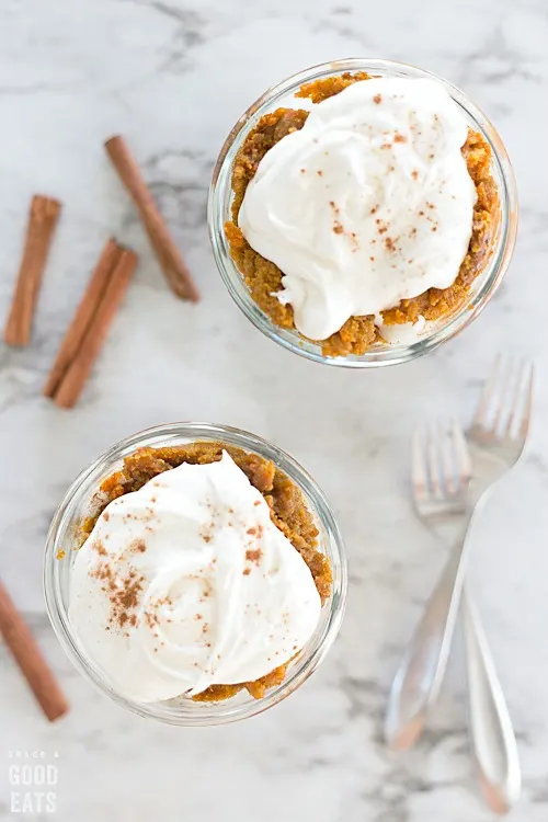 two bowls with pumpkin cake topped with cream cheese frosting next to a pair of forks and cinnamon sticks