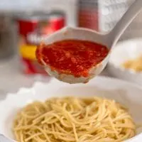 a ladle full of marinara over spaghetti noodles