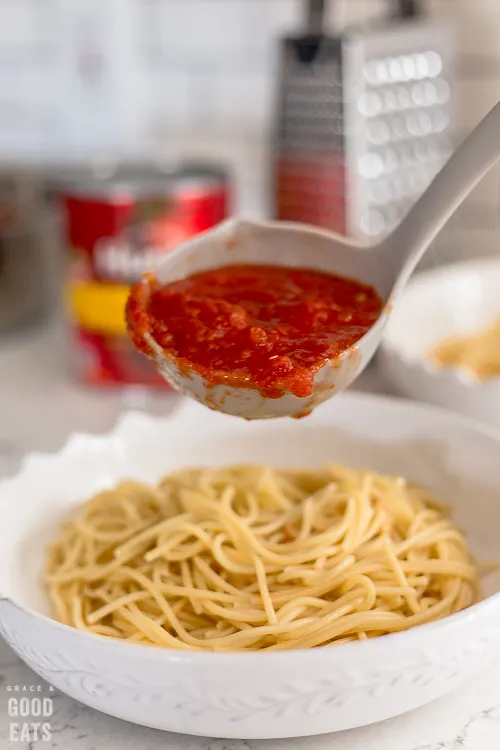 a ladle full of marinara over spaghetti noodles