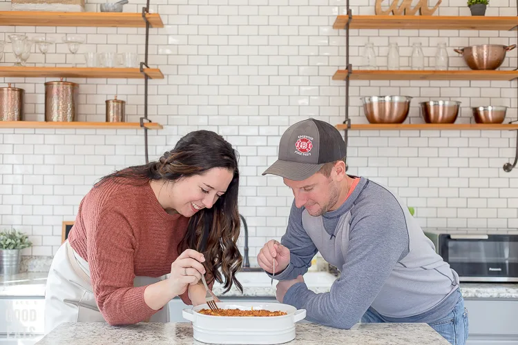 two people sharing macaroni and cheese in a kitchen