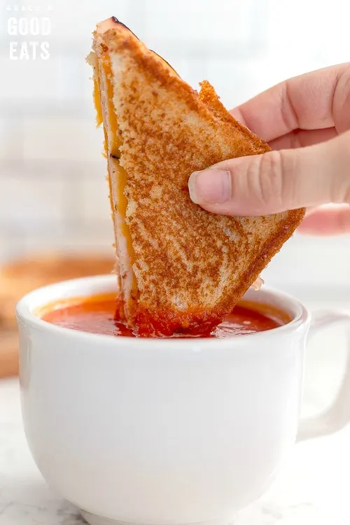 dunking a grilled cheese in a cup of instant pot tomato soup