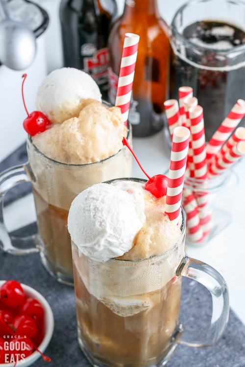 root beer floats surrounded by root beer bottles and a bowl of cherries