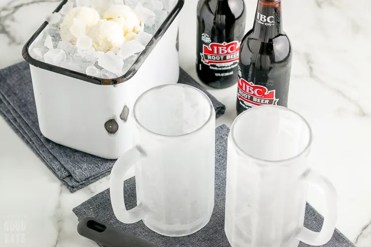 frosted mugs next to ice cream on ice and root beer bottles