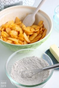 sliced peaches mixed with sugar next to a bowl of flour